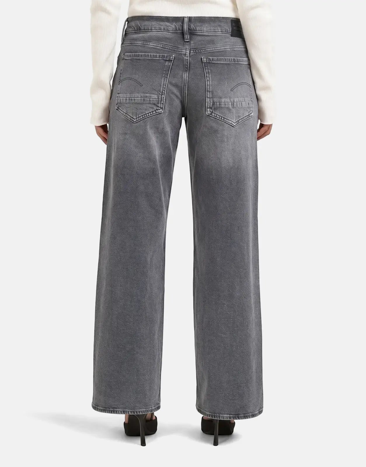 Rear view of grey faded G-Star RAW Judee loose jeans on a model, featuring distinctive back pockets and high heels.