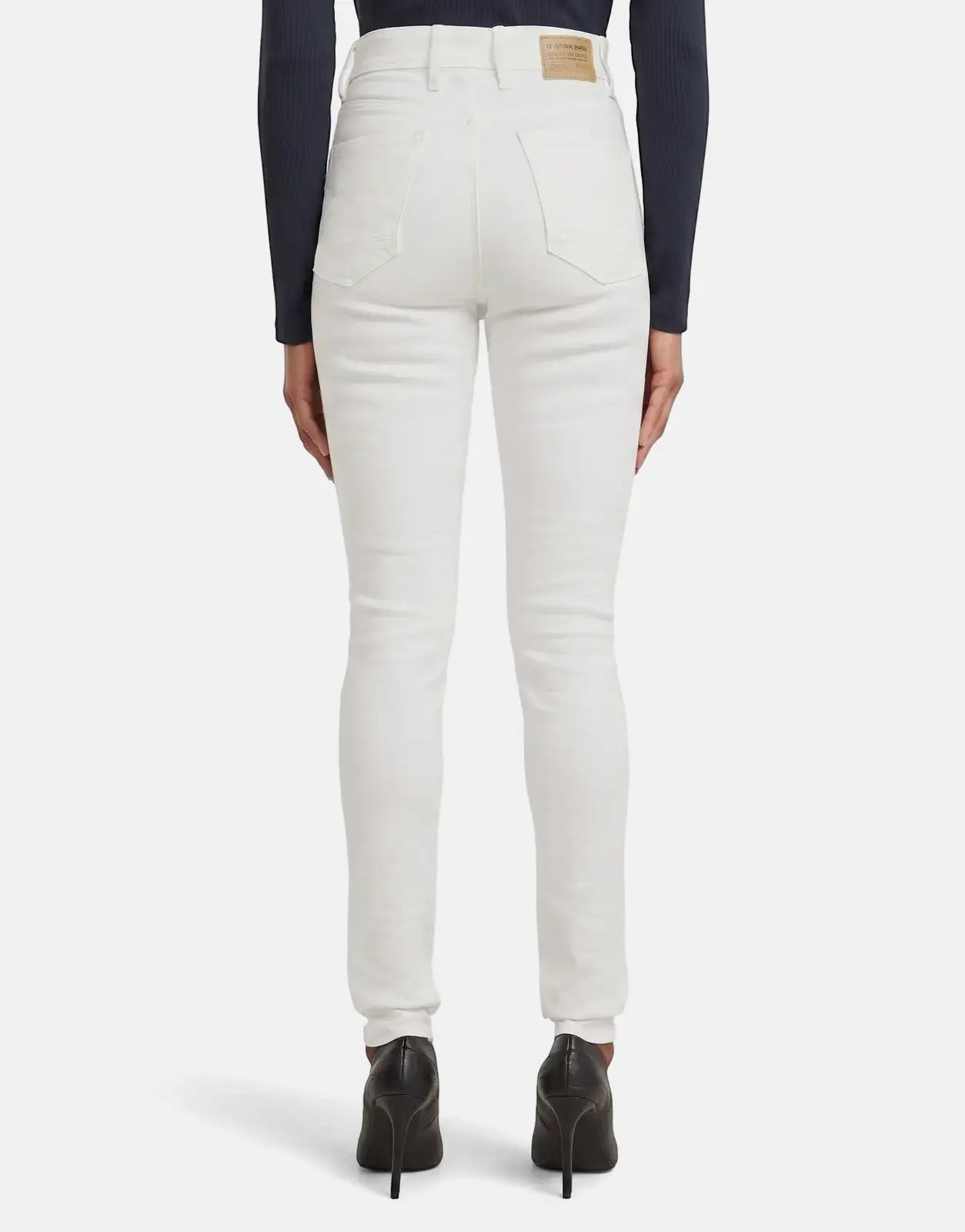 Rear view of a woman wearing white G-Star RAW Kafey Ultra High Skinny Rinsed jeans with black high heels.