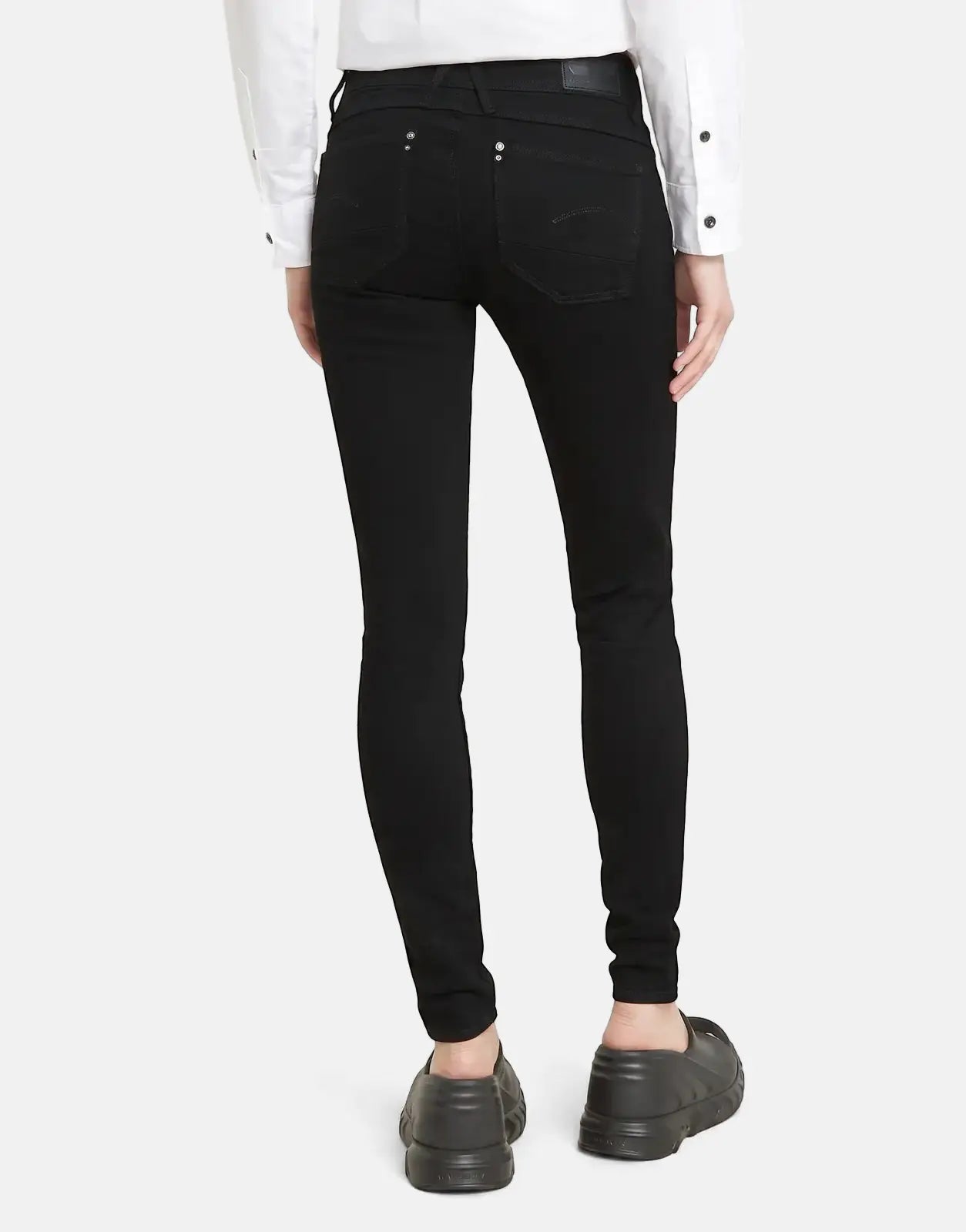 Back view of a model wearing G-Star RAW Lynn Mid Skinny Pitch Black Jeans and black clogs against a light background.