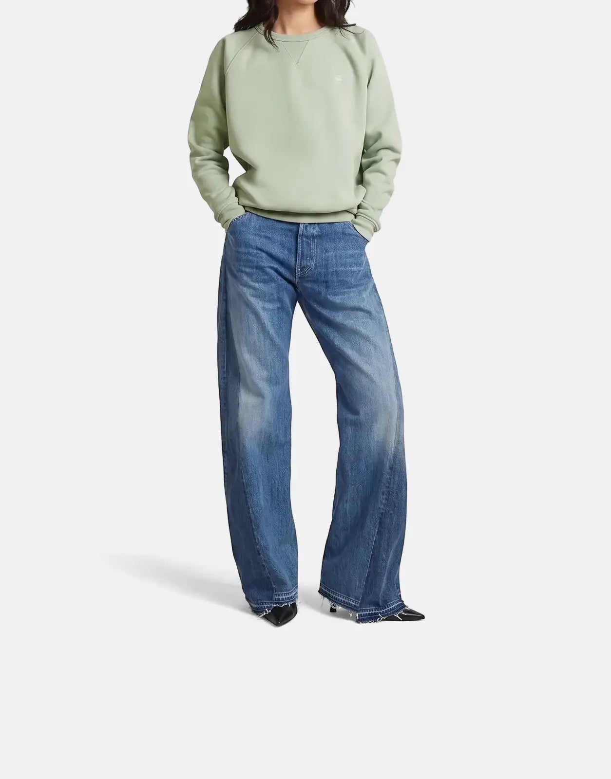 Female model wearing a G-Star RAW Premium Core 2.0 pale green sweatshirt and wide-leg blue jeans, standing facing forward.