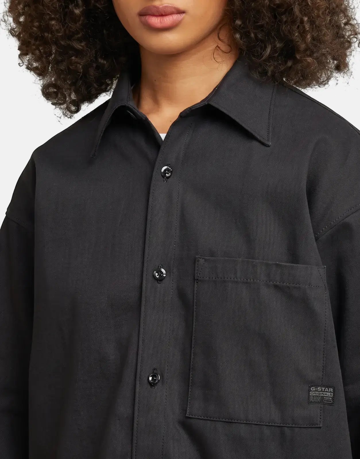 Close-up of a model wearing a black G-Star RAW Relaxed Overshirt Raw Denim, featuring a chest pocket and buttons.