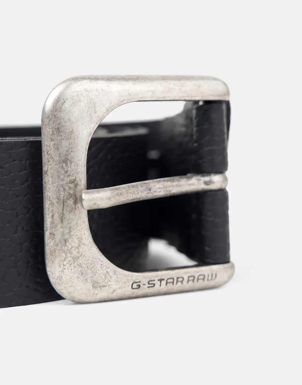 Close-up of a G-Star RAW Zed men's black leather belt with a distressed antic silver buckle featuring engraved branding.