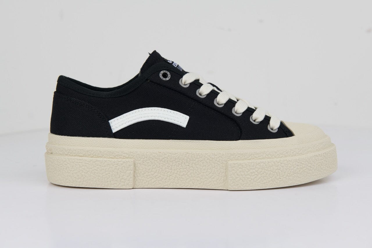 Black canvas sneakers with a white side logo, contrasting cream rubber sole, and classic lace-up design for casual wear.