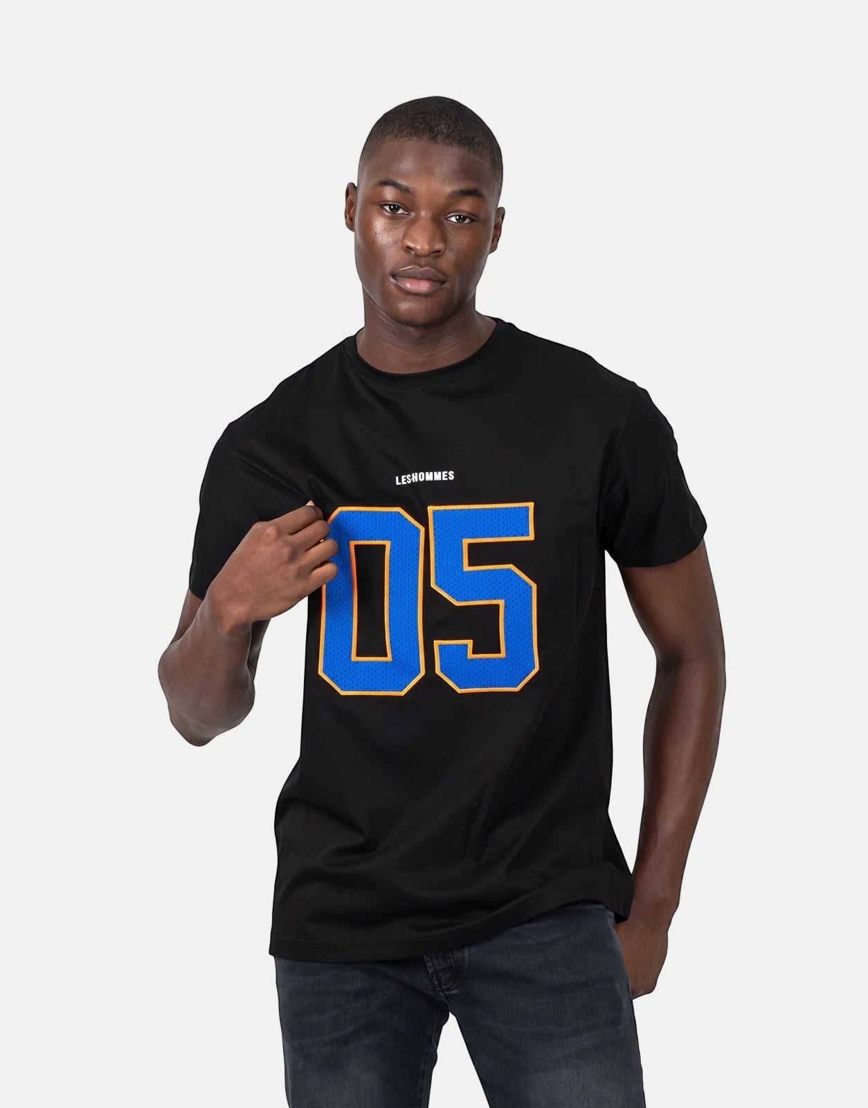 A male model wearing a black Les Hommes 05 t-shirt featuring a large blue and yellow graphic.