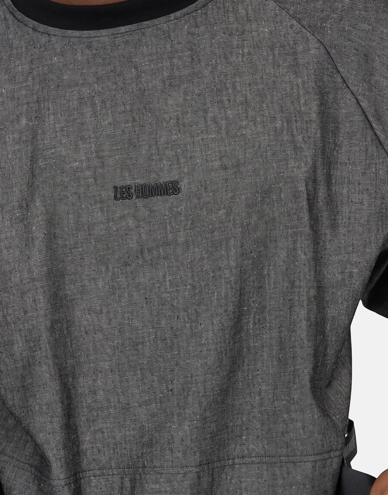 Close-up of a person wearing a grey Les Hommes t-shirt with an embroidered logo. The textured fabric and collar are clearly