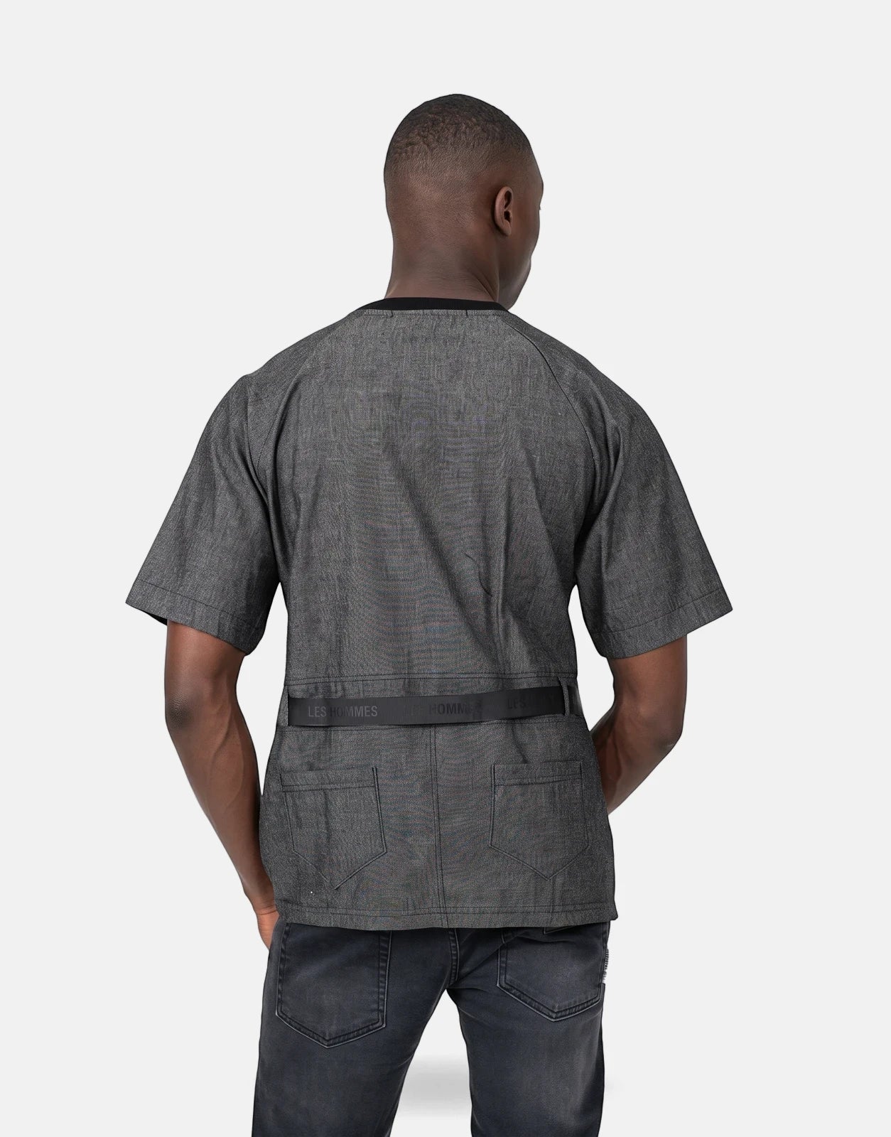 Back view of a man wearing a Les Hommes grey short-sleeved t-shirt with a black belt detail and dark grey jeans.