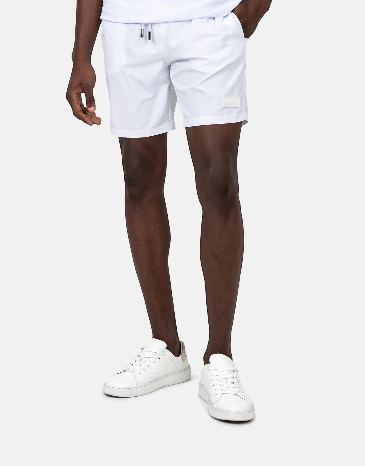 Les Hommes Colour White Swim Shorts worn by a male model with white sneakers, showcasing the product in a studio setting.