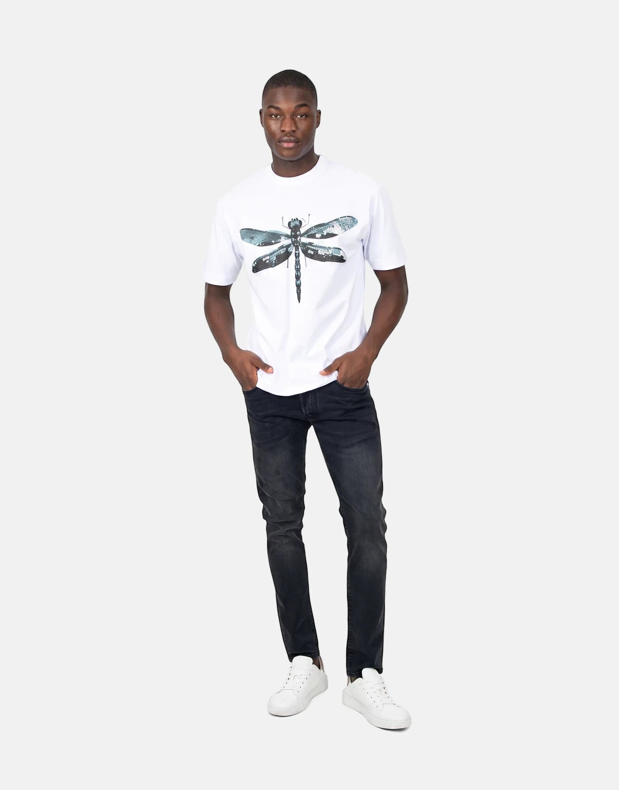 Black male model wearing a Les Hommes Dragonfly White T-Shirt paired with black distressed jeans and white sneakers.