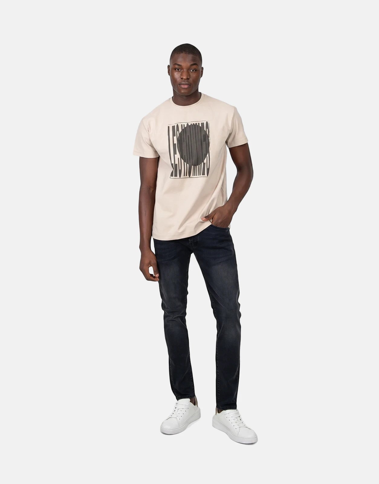 Les Hommes Logo Print Brown T-Shirt on a male model wearing dark jeans and white sneakers, full body shot.