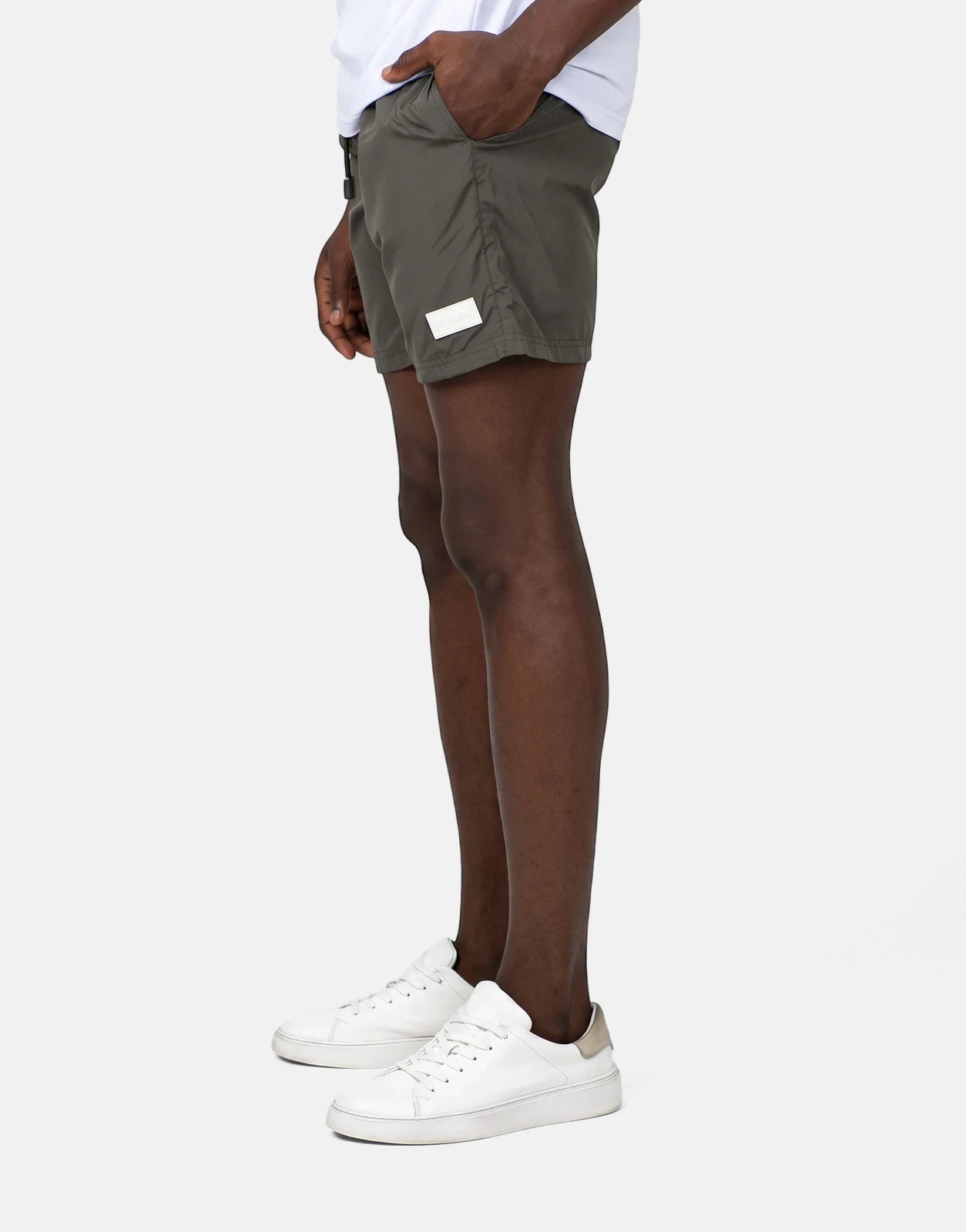 Les Hommes men's olive green swim shorts with a white logo label, styled on a model wearing white sneakers.
