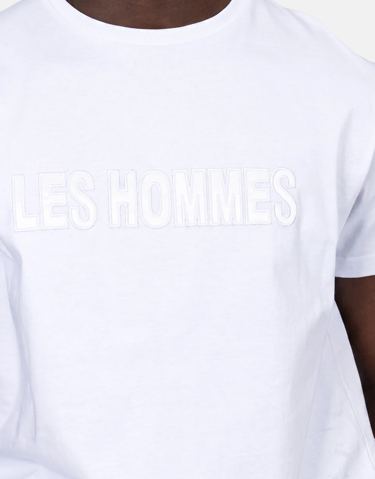 Close-up of a men's Les Hommes white t-shirt featuring an embroidered 'LES HOMMES' glitter logo on the chest.
