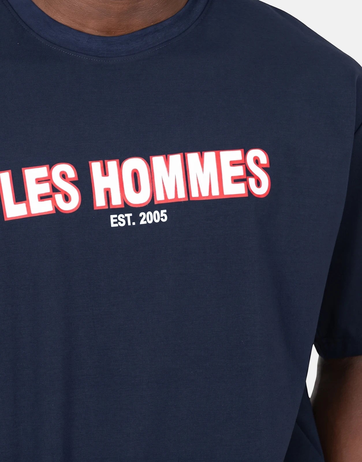 Close-up of a men's Les Hommes navy blue t-shirt featuring a distinctive white and red 'LES HOMMES EST. 2005' rubber print