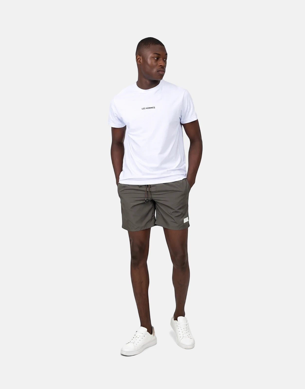 Les Hommes olive green swim shorts worn by a male model with a white t-shirt and white sneakers, full body view.
