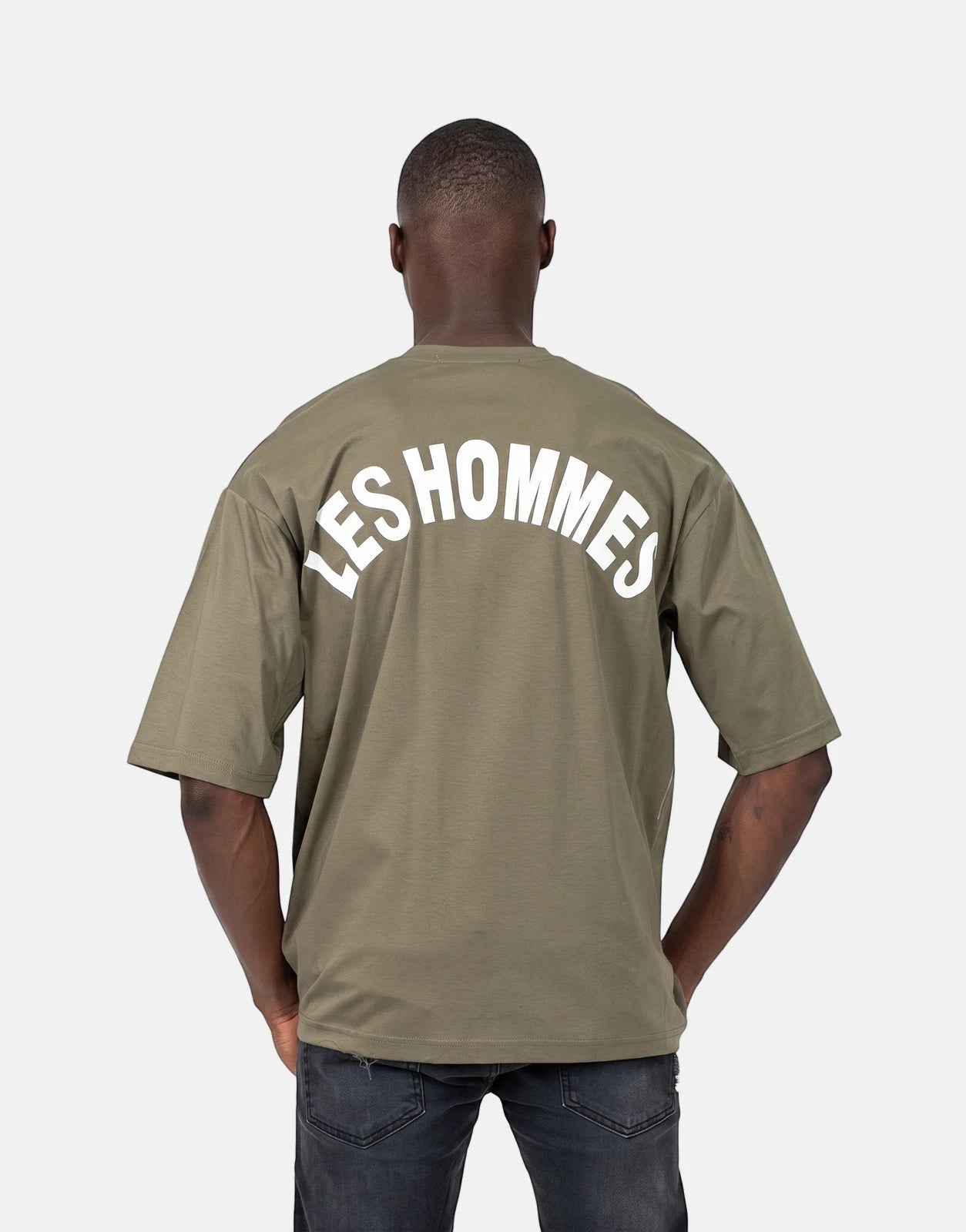 A male model wearing a green Les Hommes t-shirt with a white 'LES HOMMES' logo across the back, viewed from behind.