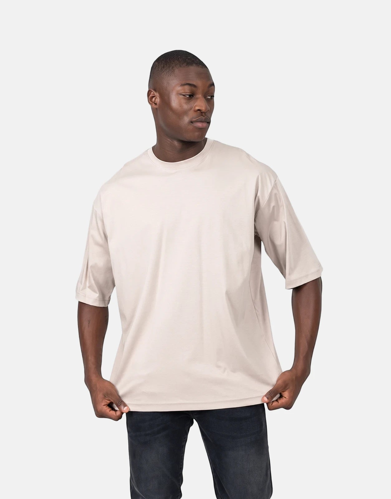 Les Hommes oversized short-sleeve t-shirt in light beige, worn by a Black male model, with dark wash jeans, studio shot.
