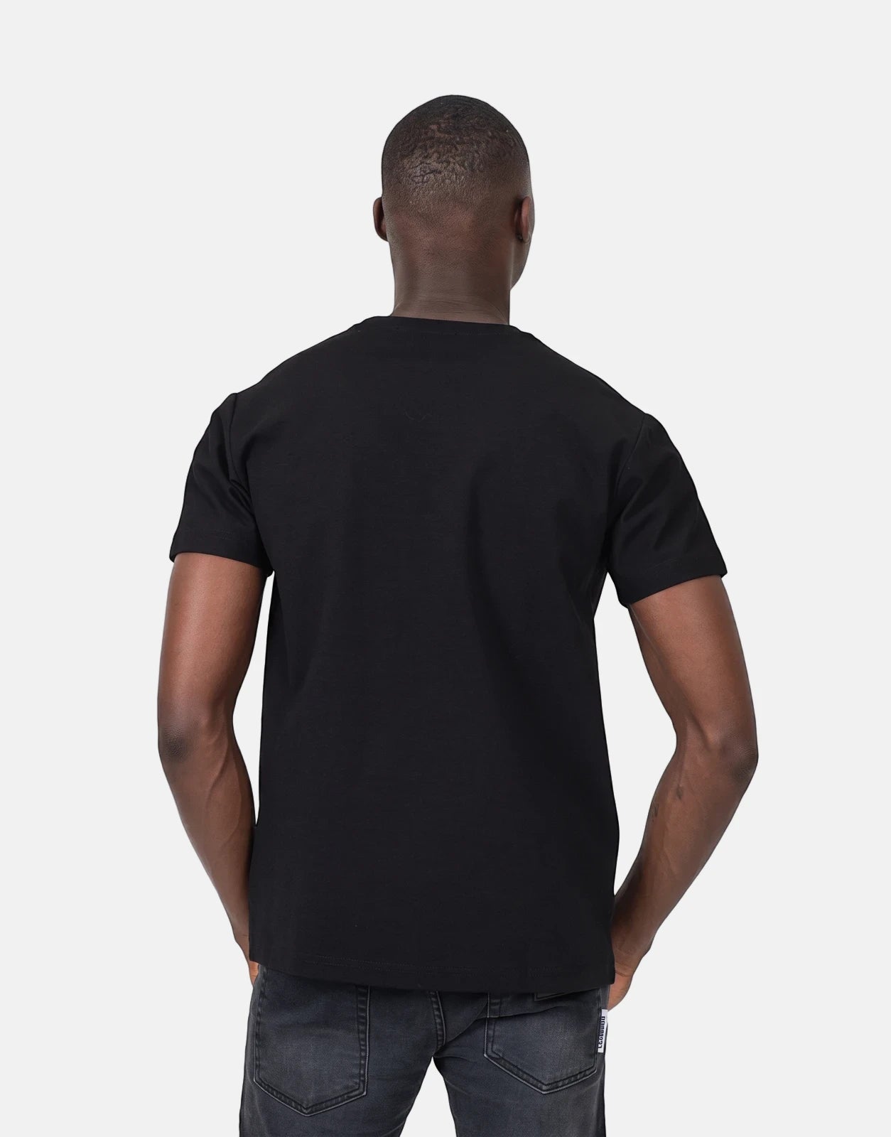 Back view of a Black man wearing a plain black Les Hommes t-shirt and dark grey jeans in a studio shot.