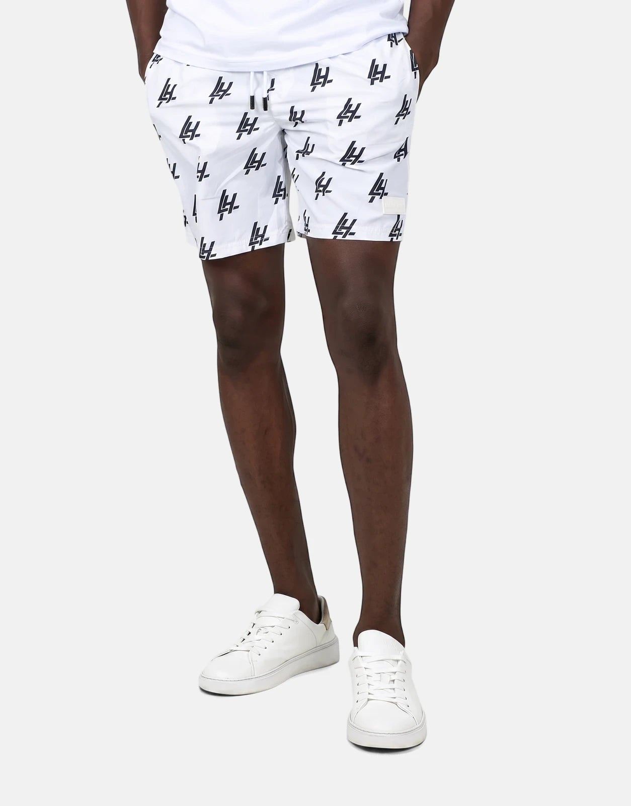 Les Hommes white swim shorts with black print on a standing model, showcasing the fit and details of the swimwear.