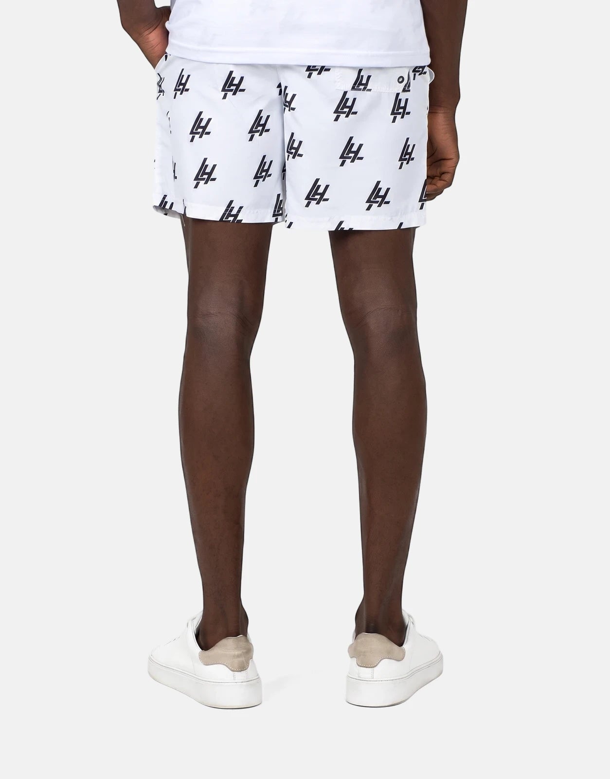 Les Hommes white swim shorts with black logo print, worn by a man from behind, paired with white sneakers.