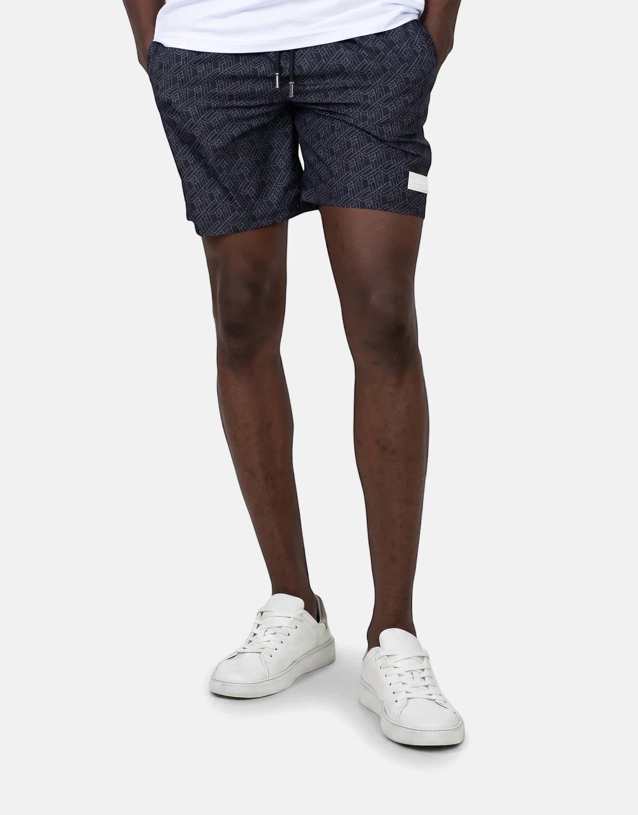 Less Hommes AOP Black Swim Shorts on a male model, showcasing the geometric print and drawstring waist.