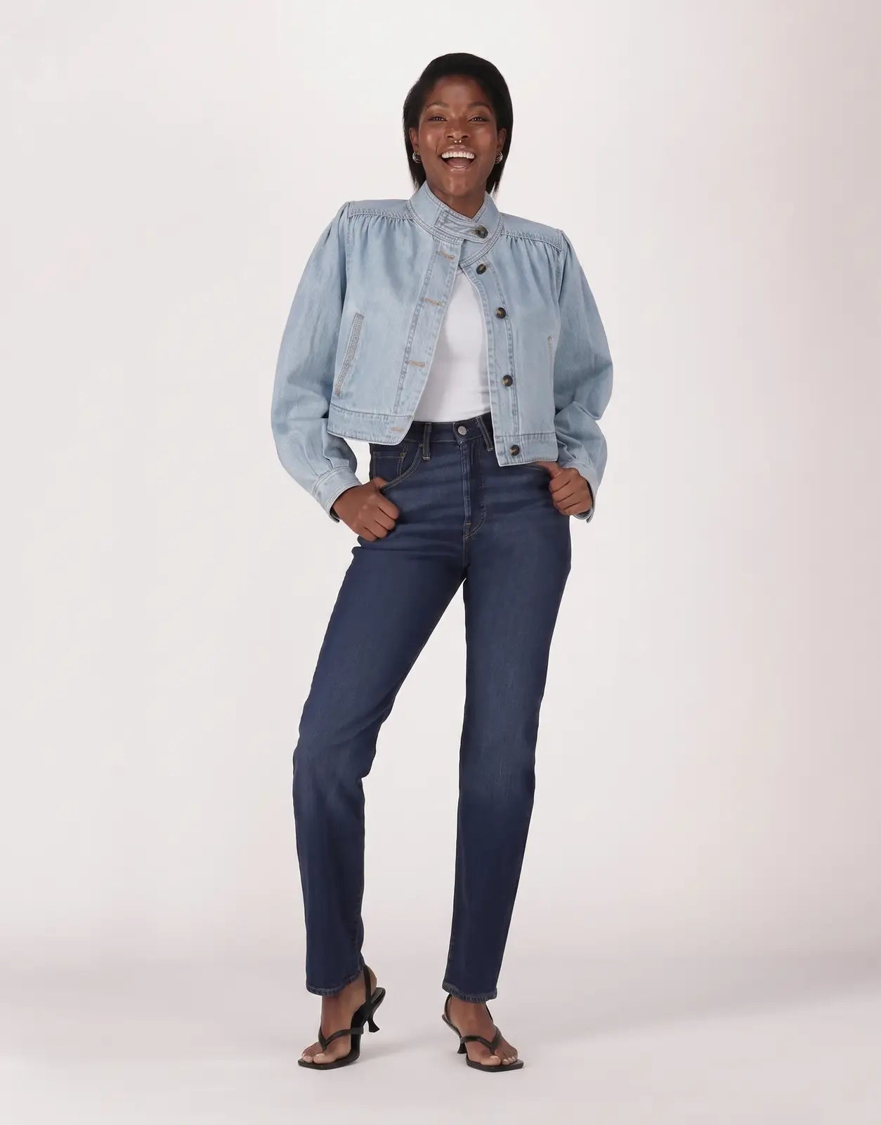 A smiling model wears Levis 501 Ladies Time Take Jeans in dark blue with a light wash denim jacket, full body shot.