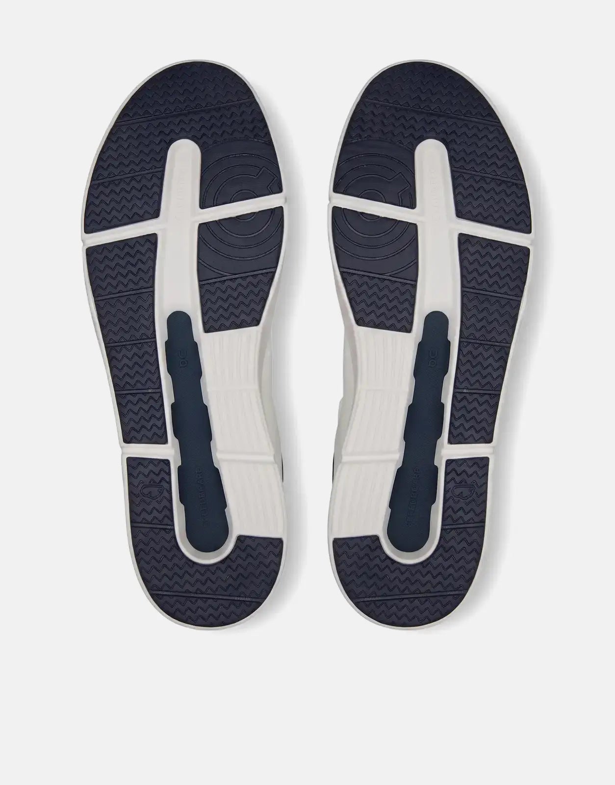 View of the soles of two white and navy blue On Men's The Roger Advantage sneakers with detailed tread.