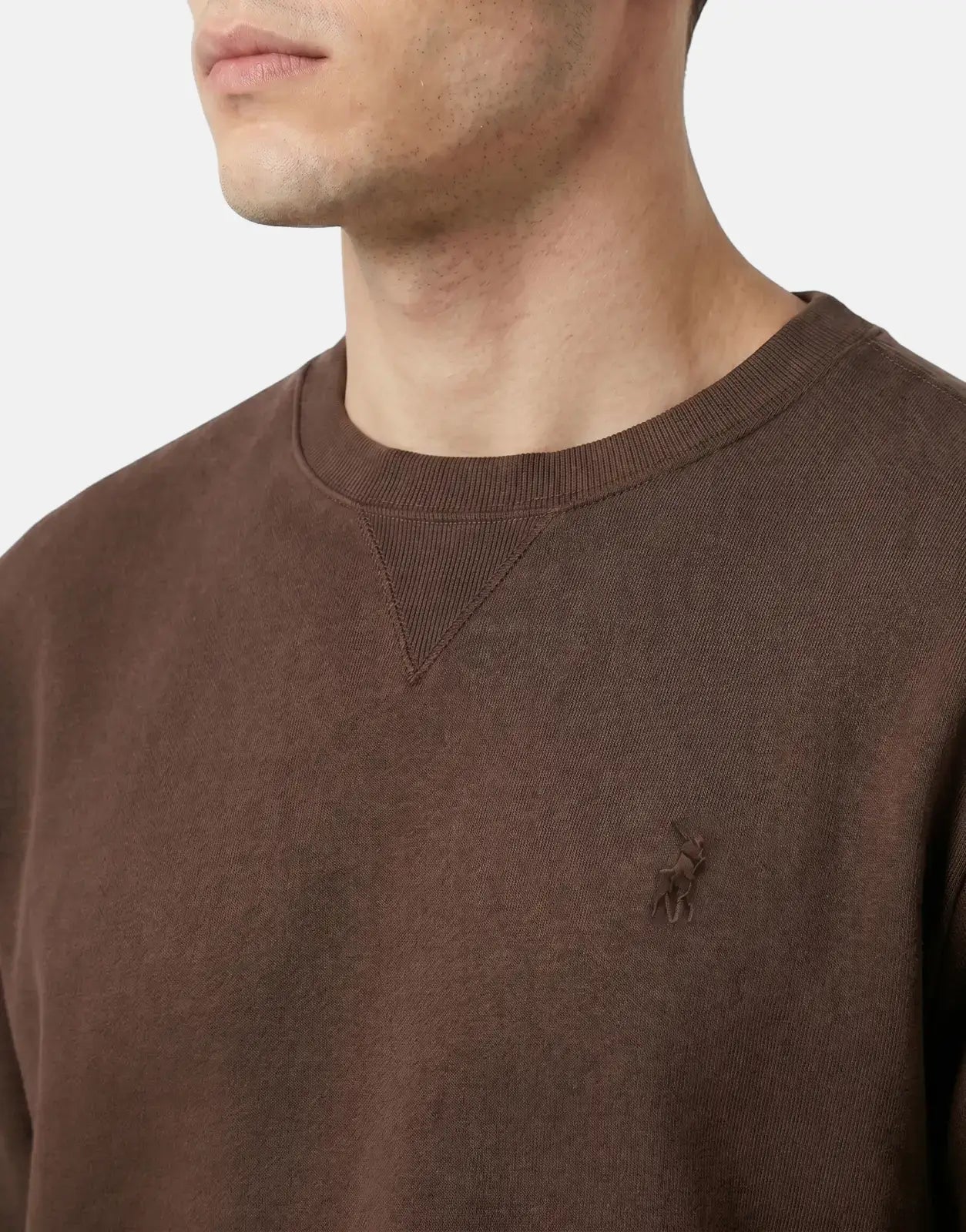 Close-up of a man wearing a brown Polo Essential Fleece Sweatshirt, showcasing the ribbed crew neck and embroidered logo.