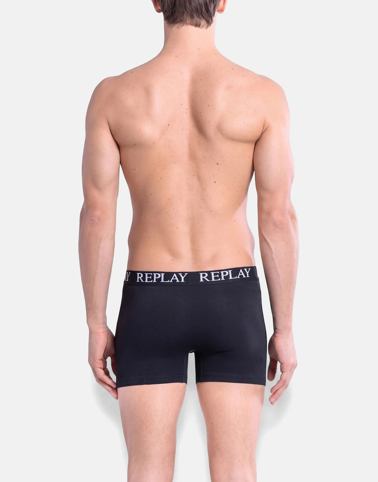 Male model from behind wearing black Replay boxer briefs against a light background, showcasing the brand's logo.