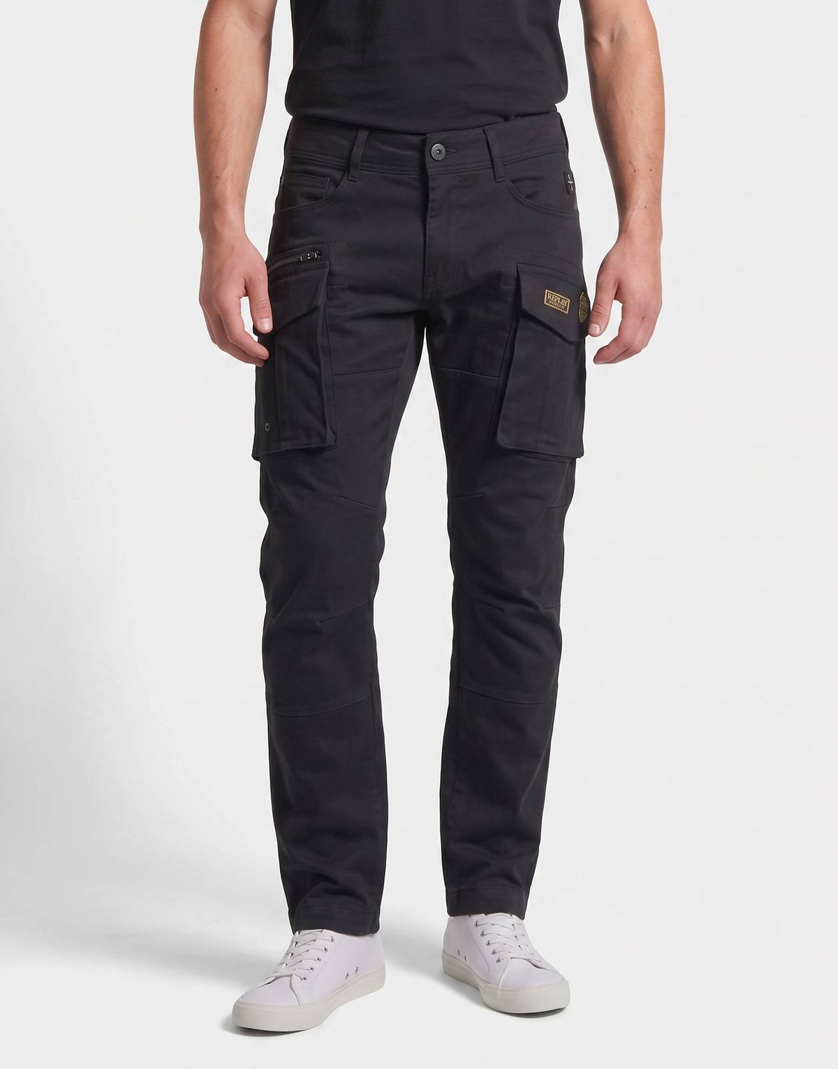 Front view of a male model wearing Replay Badges black cargo pants and a black t-shirt, standing.