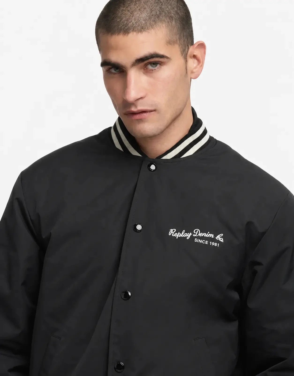 Replay Varsity Black Jacket shown from the front in black with snap buttons, striped rib collar, and chest logo.