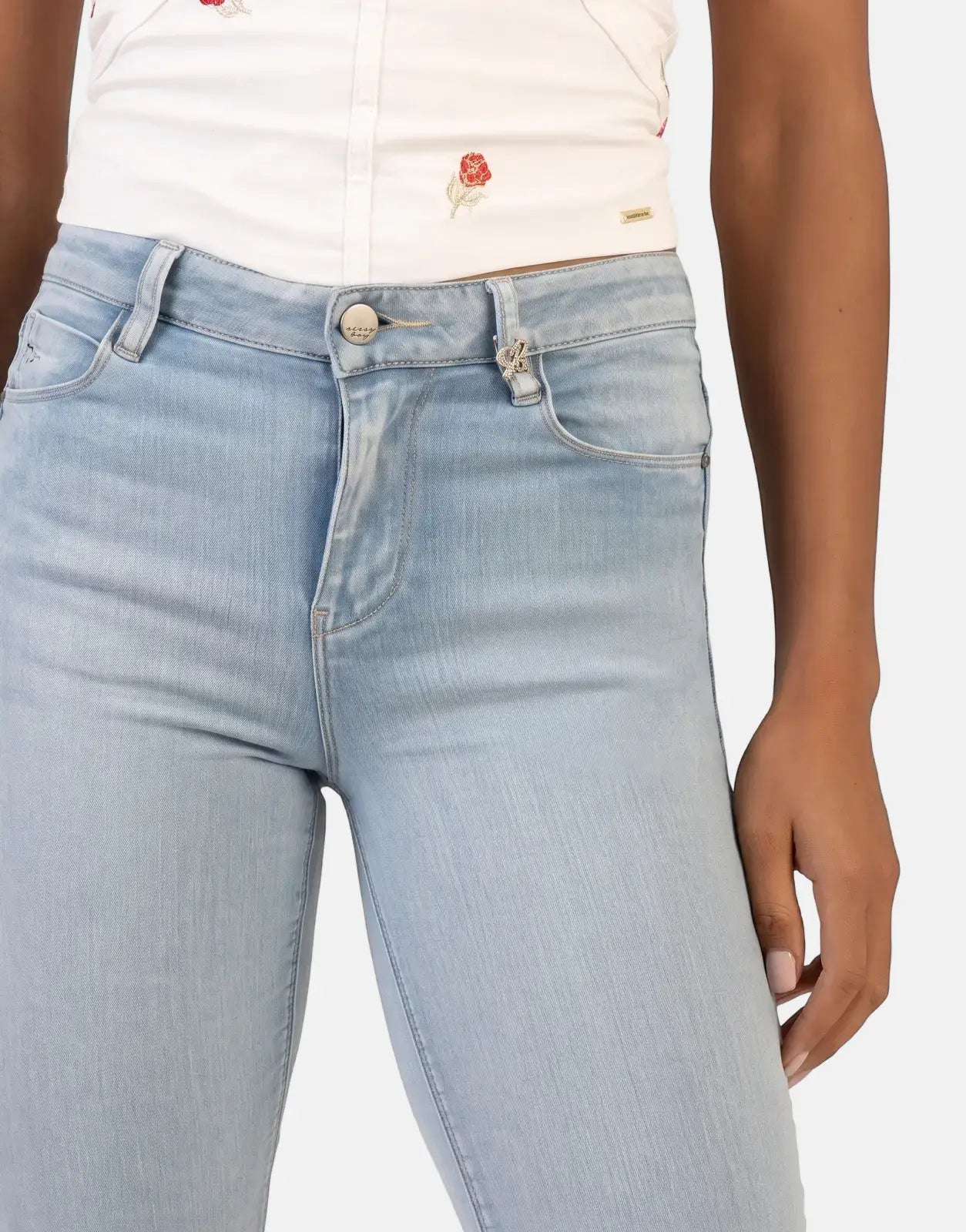 A close-up of a person wearing Sissy Boy Cara Light Vintage Mid Waist Skinny Jeans with a white embroidered top, showing