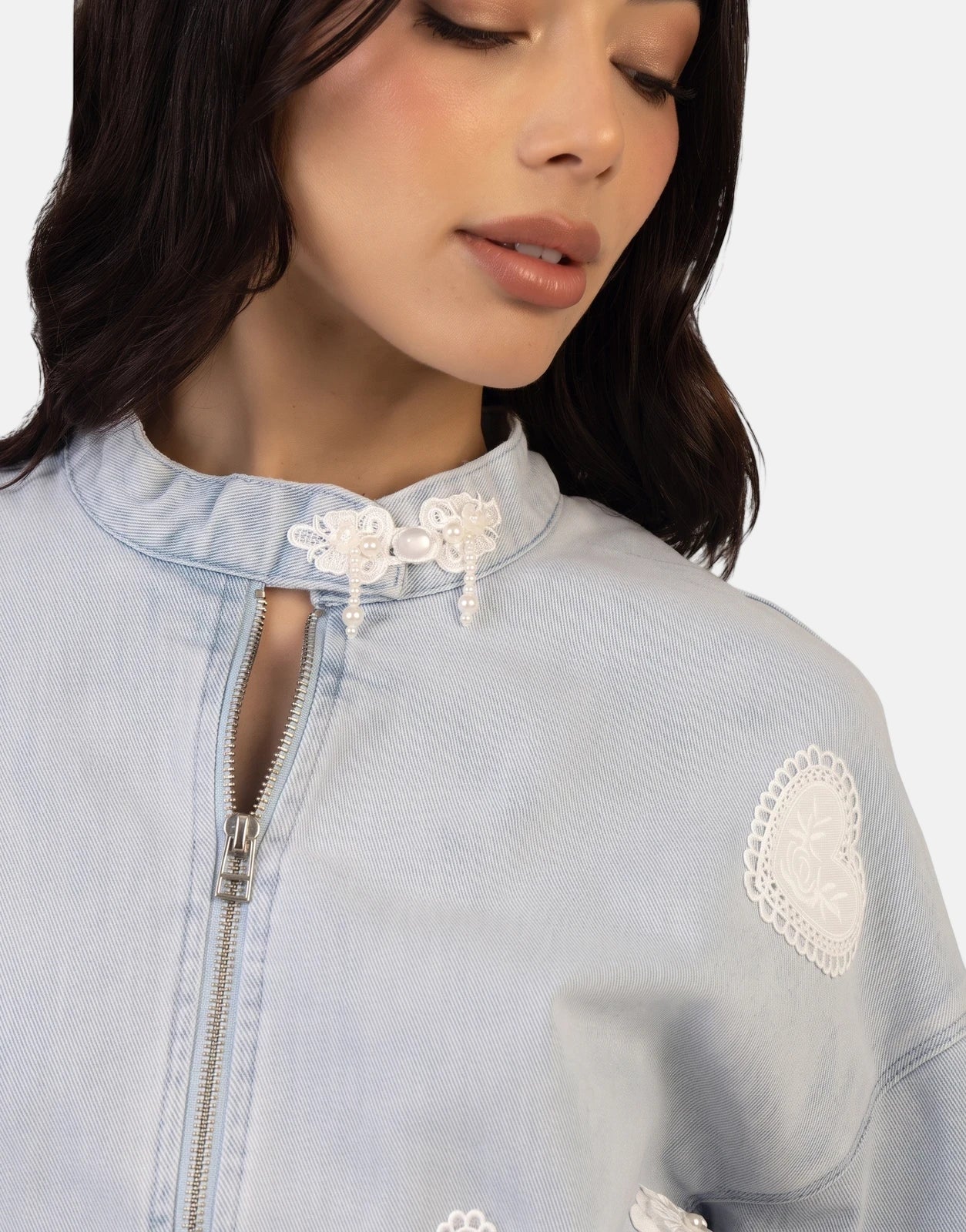 Close-up of a woman in a Sissy Boy Kiera Light Vintage Denim Bomber Jacket with white lace, pearl embellishments, and a