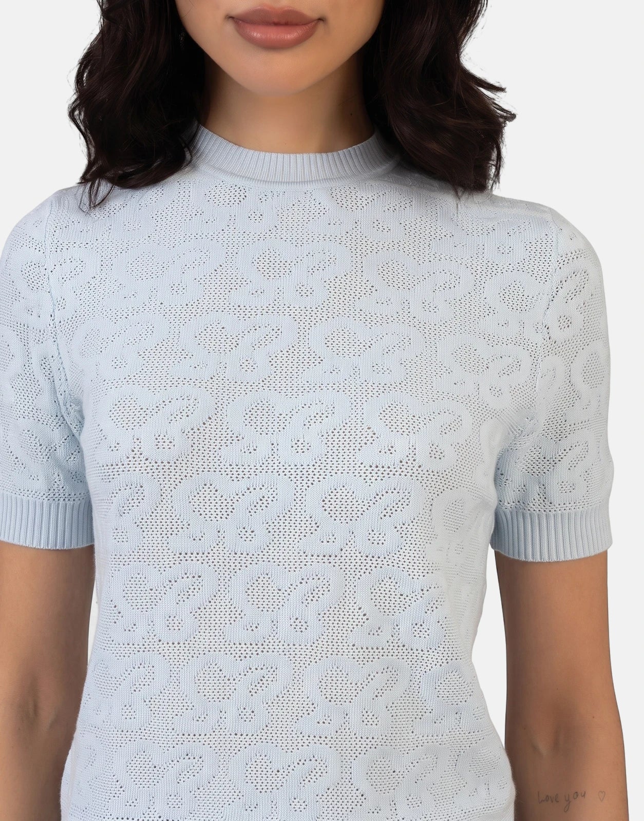 Close-up of a woman wearing a Sissy Boy Next Level pale blue knit top with a detailed openwork pattern and short sleeves.