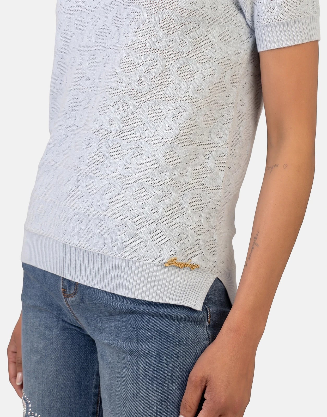 Sissy Boy Next Level Pale Blue Knit Top for women, featuring a patterned knit, short sleeves, and worn with blue jeans.