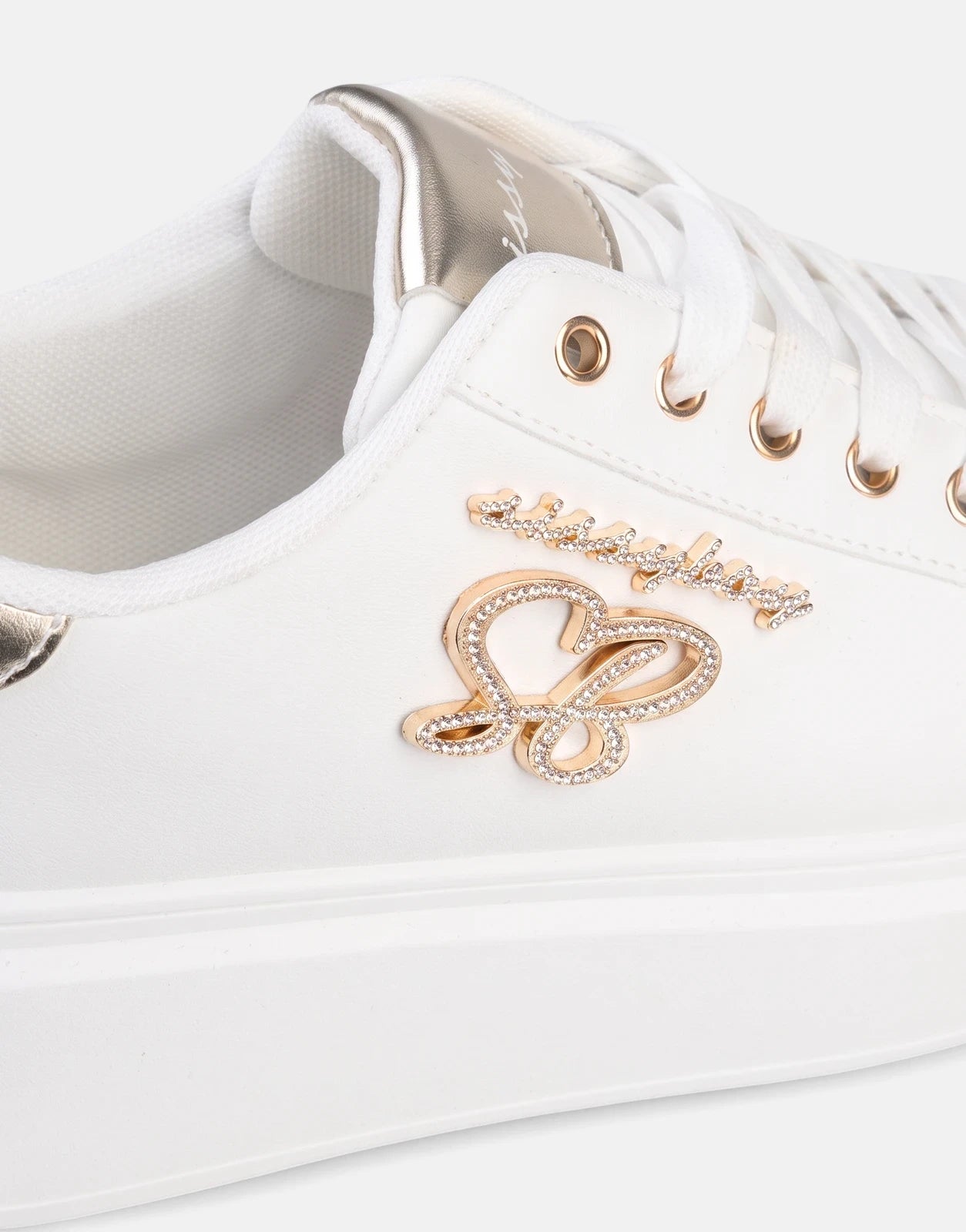 Close-up of a white Sissy Boy Noella sneaker featuring gold eyelets, white laces, and dazzling gold and diamond-like emblem