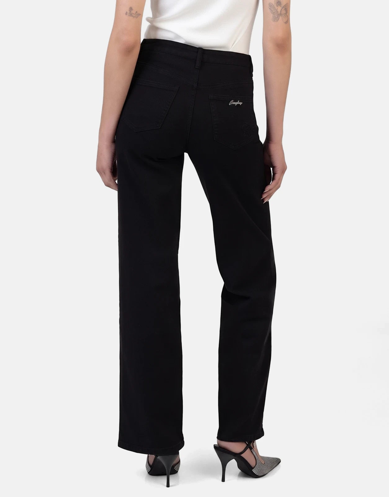 Rear view of Sissy Boy Nollene wide leg high waist black denim jeans on a female model wearing studded heels.