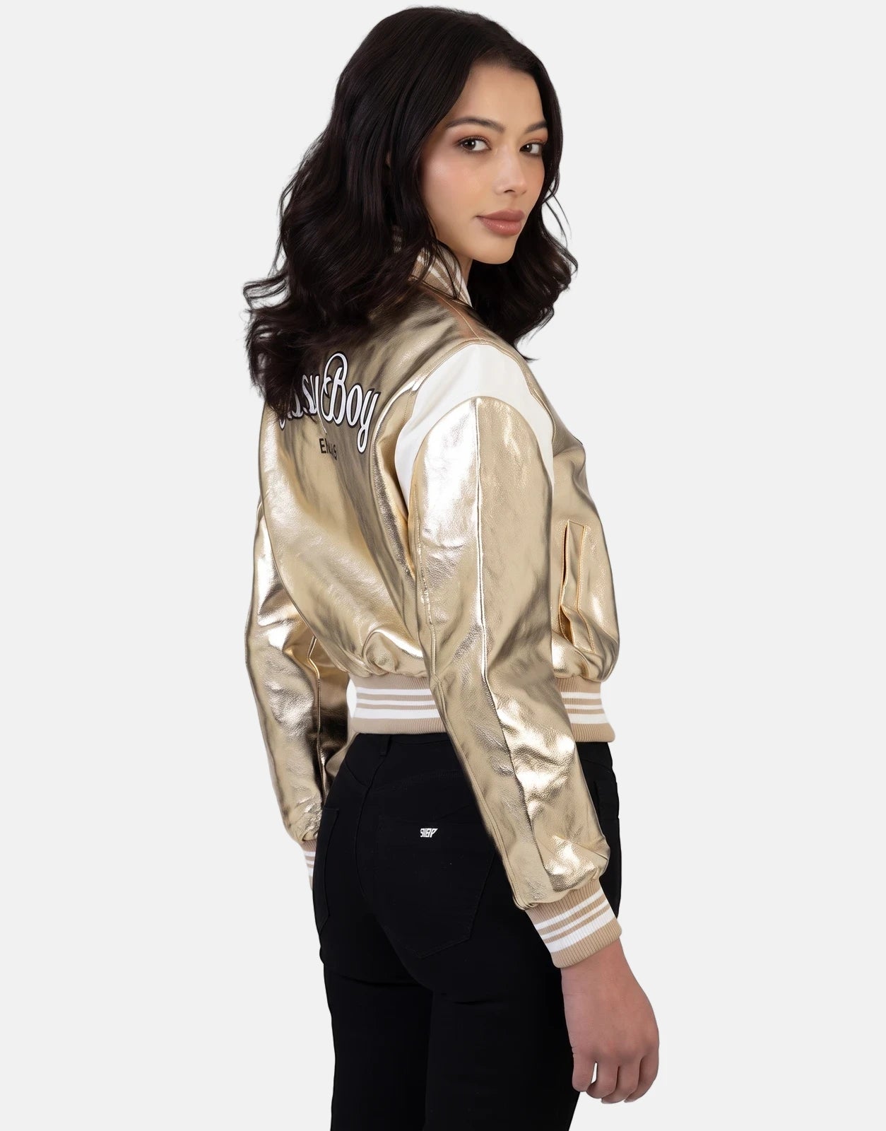 Young woman wearing a Sissy Boy Take It Easy gold metallic bomber jacket with white panels and black pants, looking over her