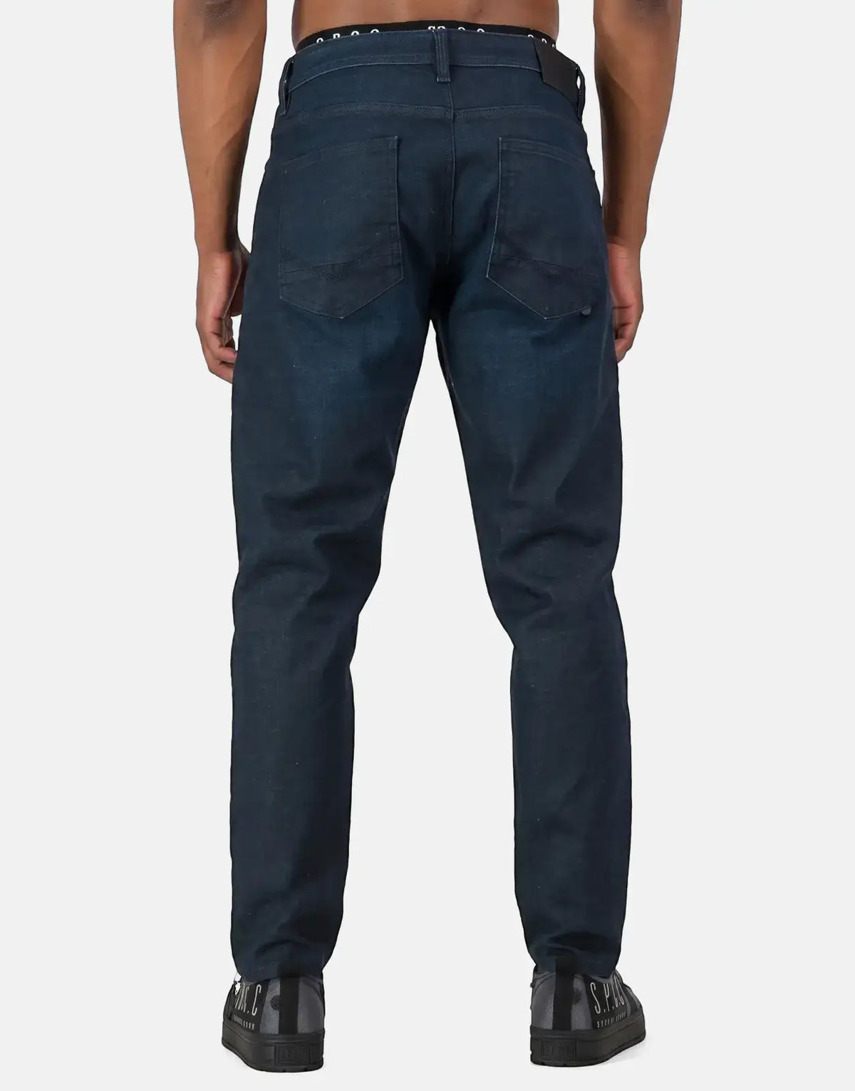 Dark blue men's SPCC Aphotic jeans, shown from the back, with a clear view of the back pockets and sneaker detailing.