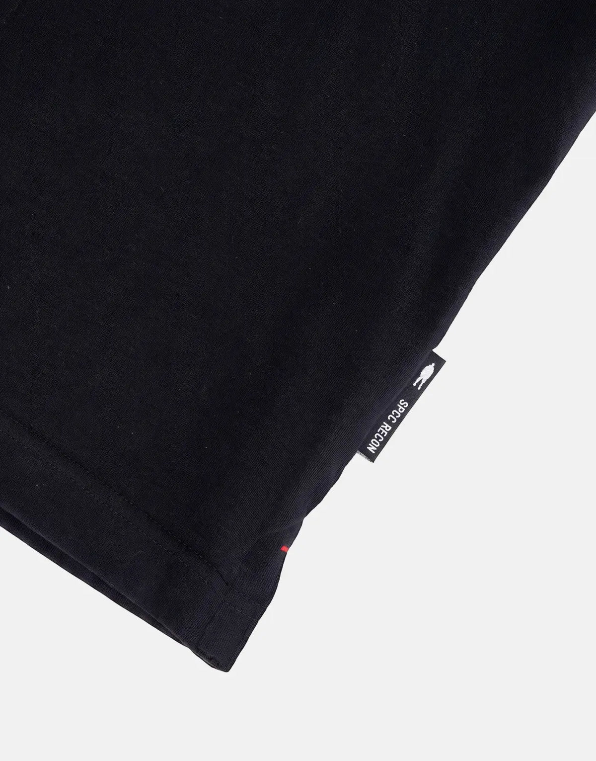 Close-up view of the hem and woven label on a black SPCC Recon Overwatch T-shirt, showing the brand logo.