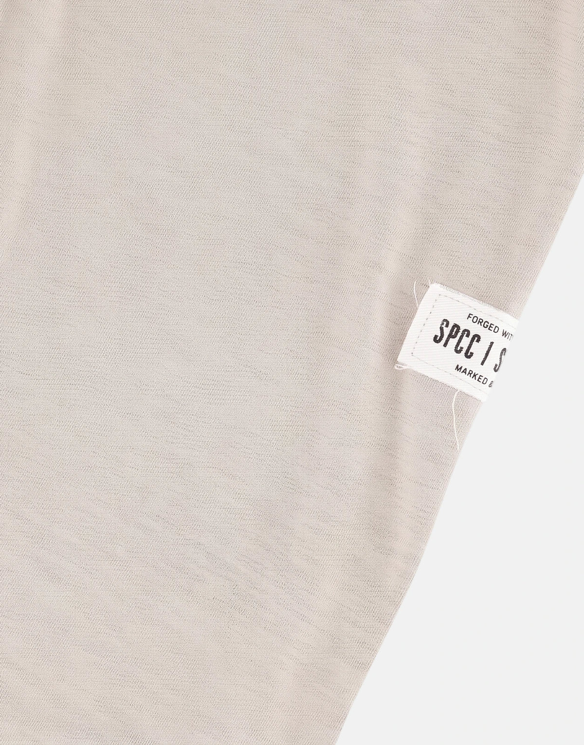 Close-up view of a light beige SPCC Troy Tee fabric with a visible SPCC brand label stitched on the corner.