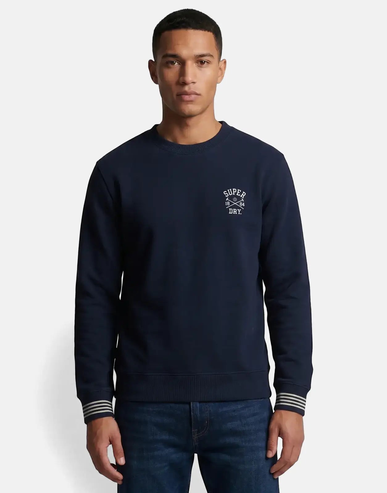 Male model wearing a navy Superdry Athletic Club crew neck sweatshirt with white logo and striped cuffs, paired with blue