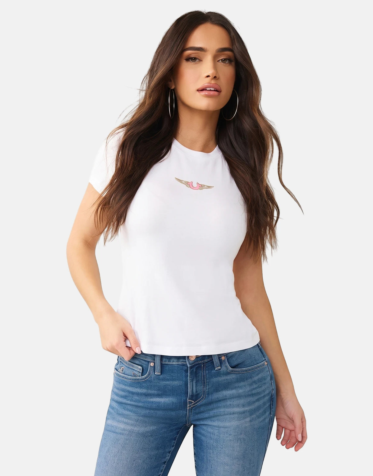 Woman models a white True Religion HS Wing T-Shirt with a pink and gold wing logo, paired with blue jeans, against a white