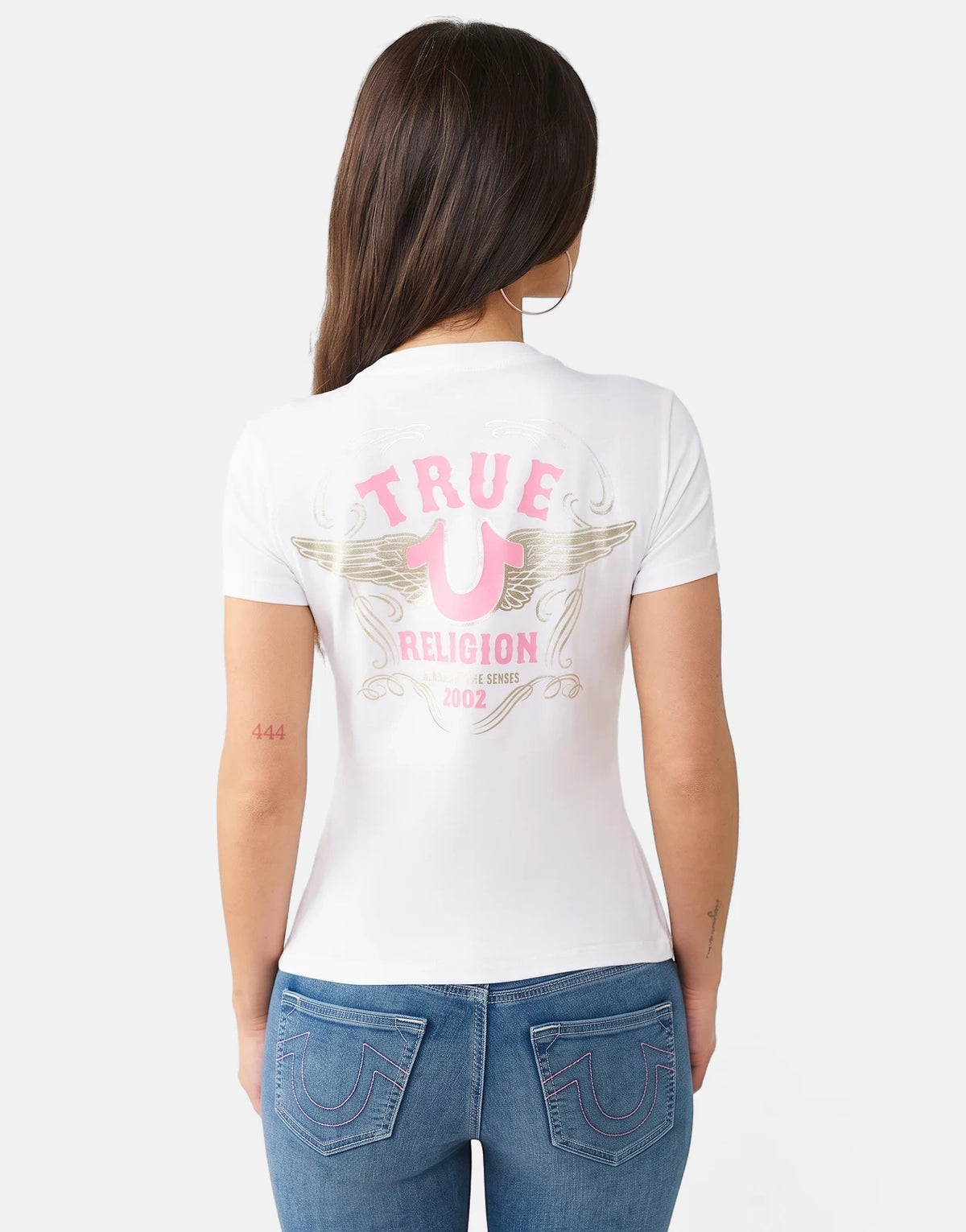 True Religion HS Wing T-Shirt in white, featuring a distinctive pink and gold wing logo on the back, worn by a woman.