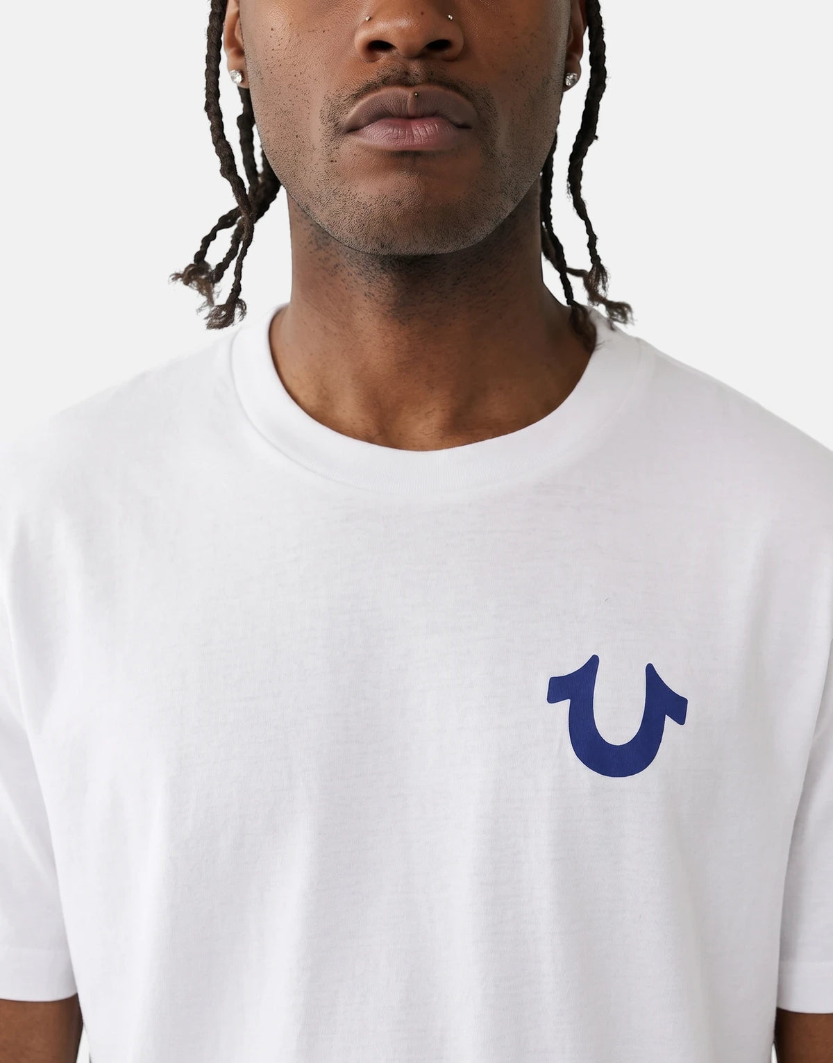 Man wearing a white True Religion TR Rect T-Shirt with a blue horseshoe logo on the chest, close-up shot.